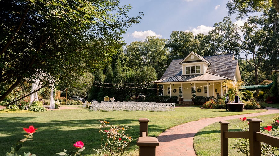 Daytime view of Alexander Homesteads farmhouse-style wedding venue with outdoor ceremony space set up on manicured lawn