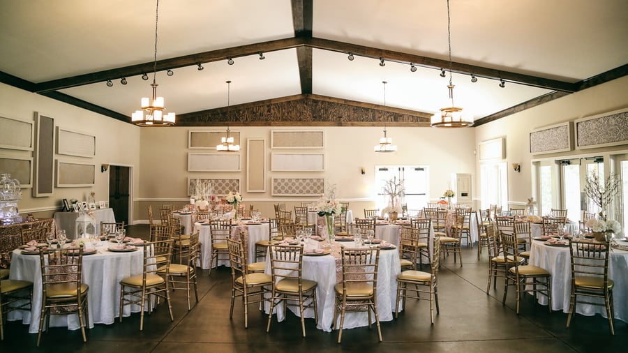 Interior view of Riverwood Manor's Grand Hall featuring vaulted ceilings with wooden beams, chandeliers, elegant table settings with white linens and gold chiavari chairs for corporate events and social gatherings - Ken Thomas Photography